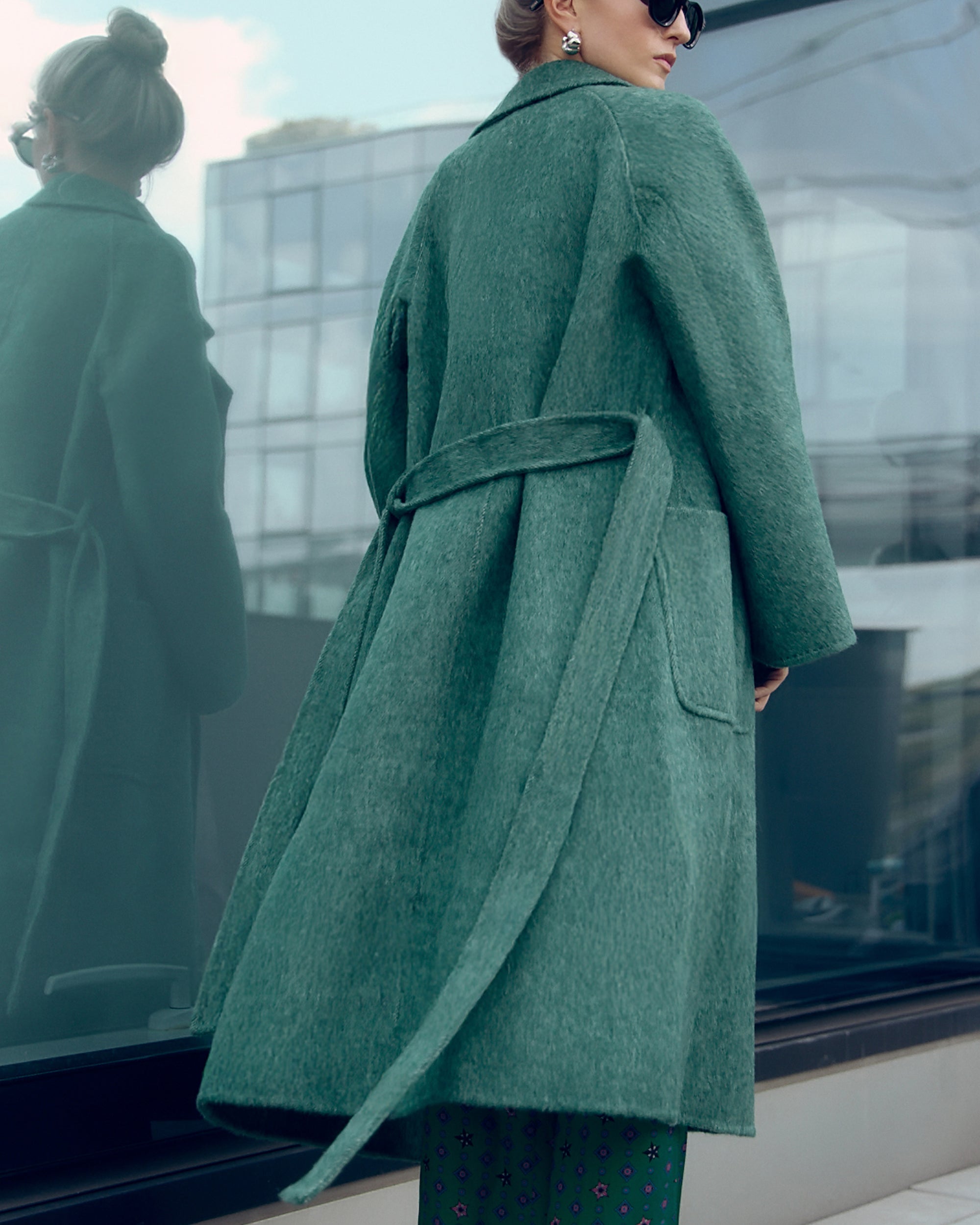 Long belted wool-blend coat in muted moss green, featuring wide lapels, oversized patch pockets, and a relaxed, robe-style silhouette. Made from a soft brushed wool and cashmere blend with a heathered texture, this timeless overcoat drapes elegantly for effortless city styling.