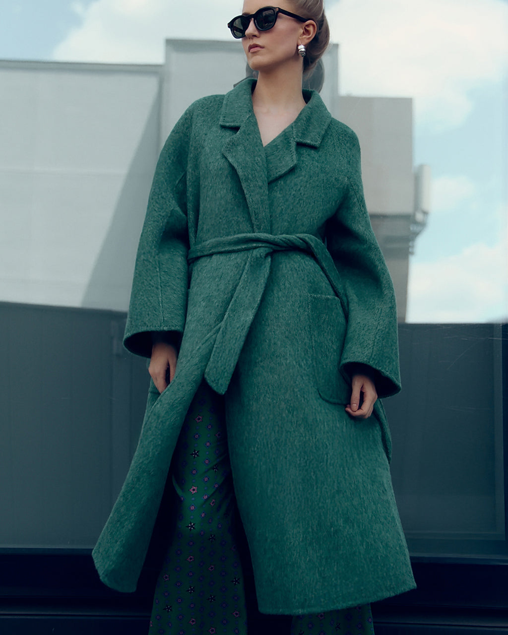 Long belted wool-blend coat in muted moss green, featuring wide lapels, oversized patch pockets, and a relaxed, robe-style silhouette. Made from a soft brushed wool and cashmere blend with a heathered texture, this timeless overcoat drapes elegantly for effortless city styling.